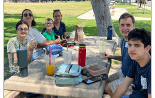 A group enjoys a picnic lunch at a park table.