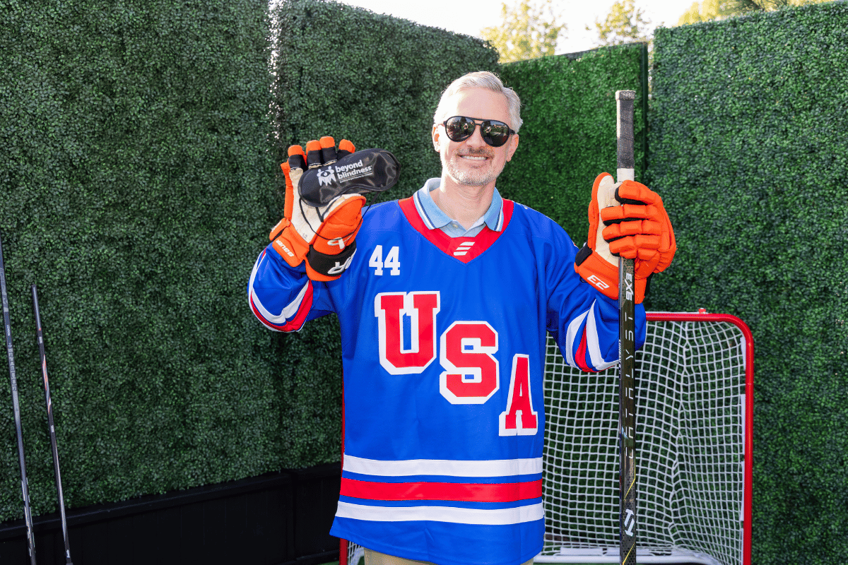 A man poses with a hockey stick and a blindfold