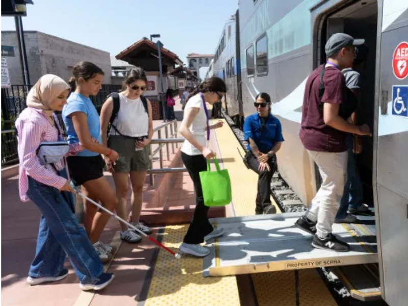 Seven people walking onto a train. One holding a white cane.